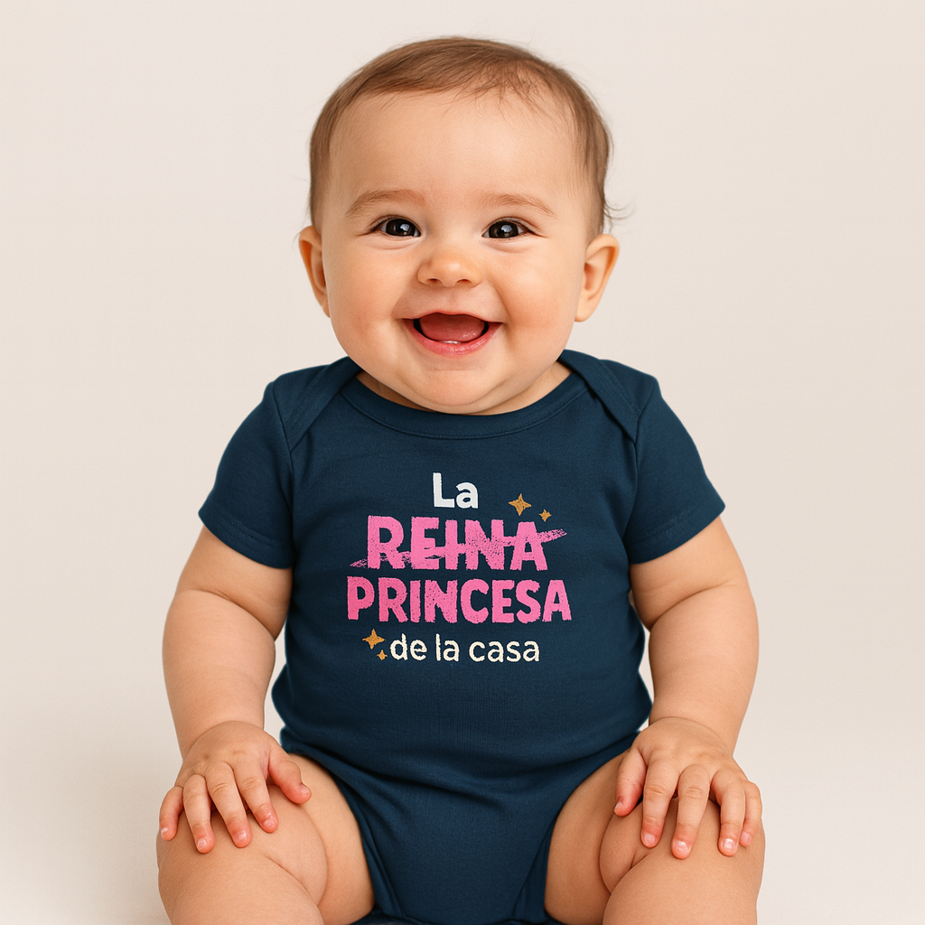 Smiling baby wearing a navy blue onesie with the Spanish text ‘La princesa de la casa’ in pink and white letters with gold stars.